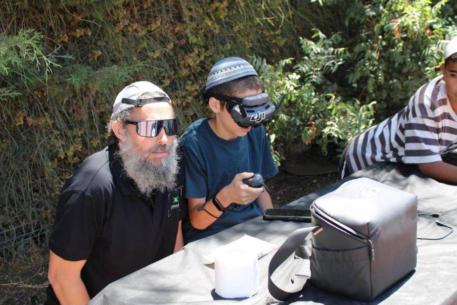 תלמיד מטיס רחפן עם משקפי FPV לצד מדריך